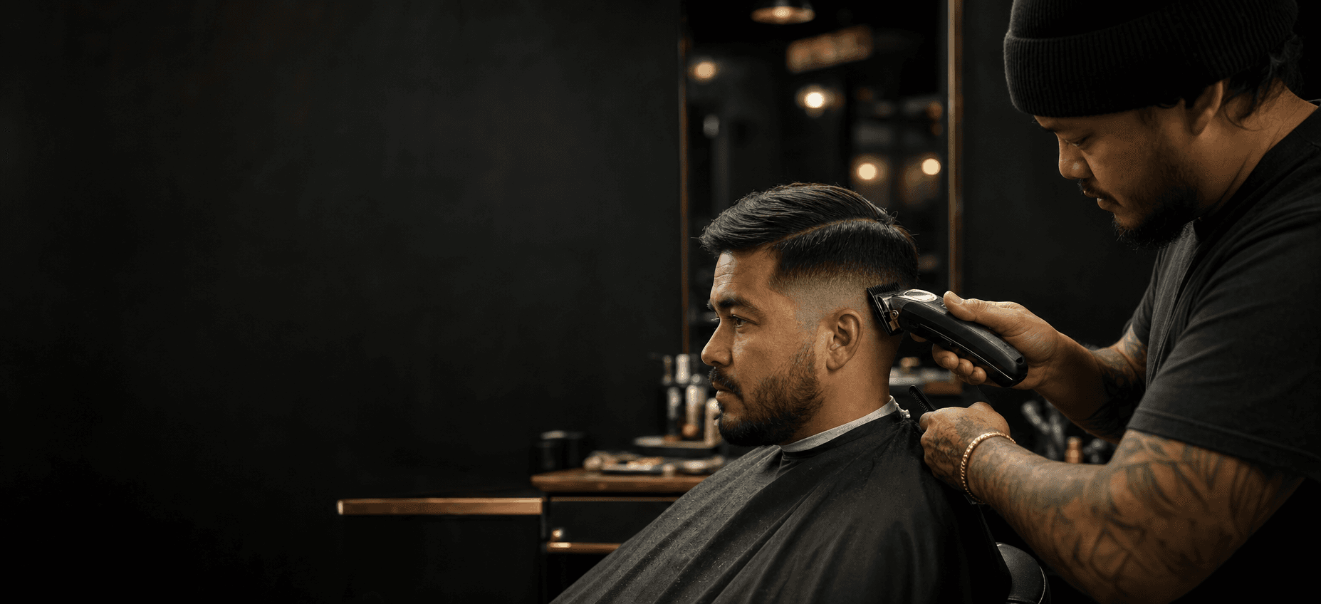 Barber shaping a precision fade in a dark modern barbershop